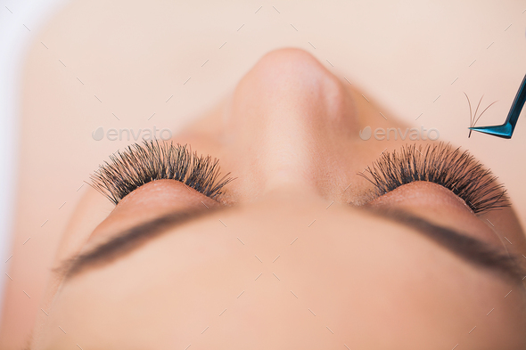 Professional stylist lengthening female lashes. Master and a client in a beauty salon.