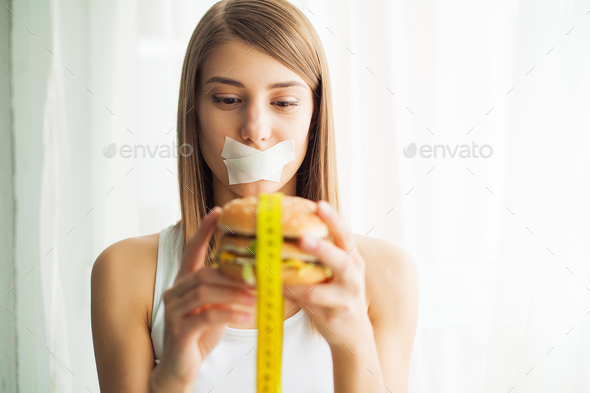Young woman with duct tape over her mouth, preventing her to eat junk food. Healthy eating concept.