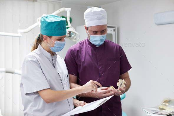 Team of dentists consulting each other about the dental treatment, holding a model of human jaw bone