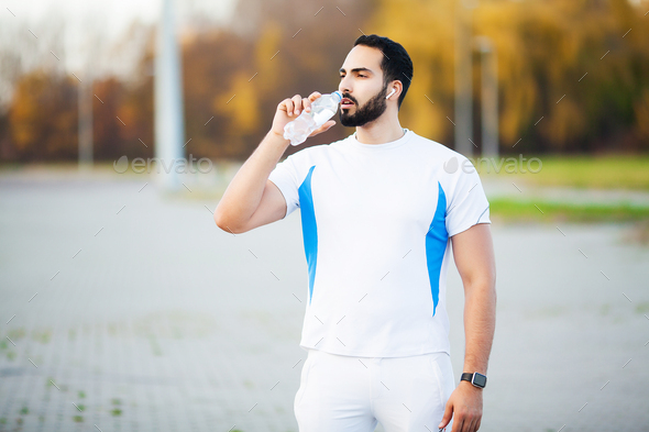 Exhausted runner man drink water on the park after workout