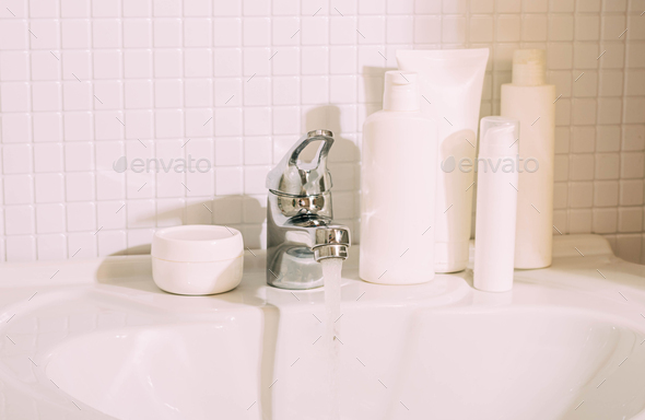 White bottles with various cosmetics stand on sink in bathroom. Cleanliness and order in the house
