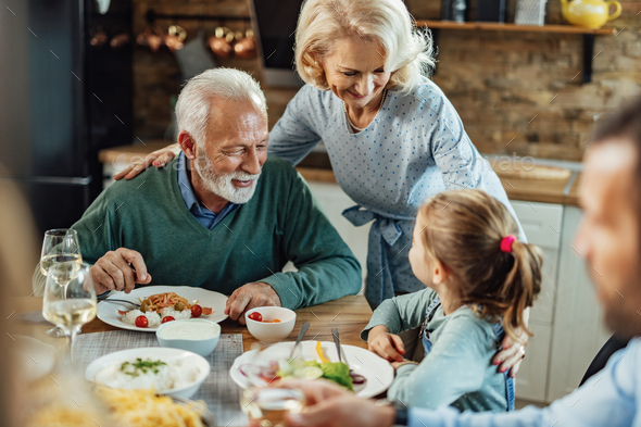 Happy grandparents talking with their granddaughter at dining table ...