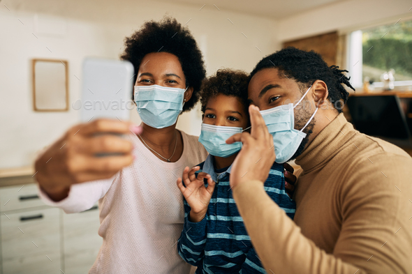 Happy African American family with face masks having video call over smart phone at home.
