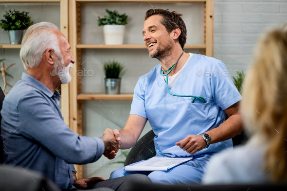 Happy doctor and mature man handshaking while greeting during a home visit. - Stock Photo - Images
