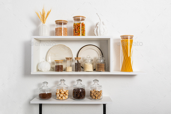 a set of glass and ceramic dishes, glass filled jars with bulk products on white kitchen shelves