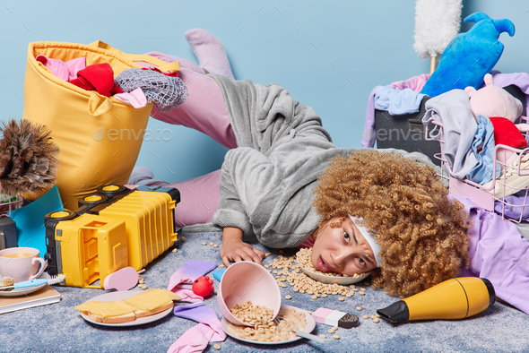 Tired exhausted woman lies on floor among different items and food thinks of many tasks to do