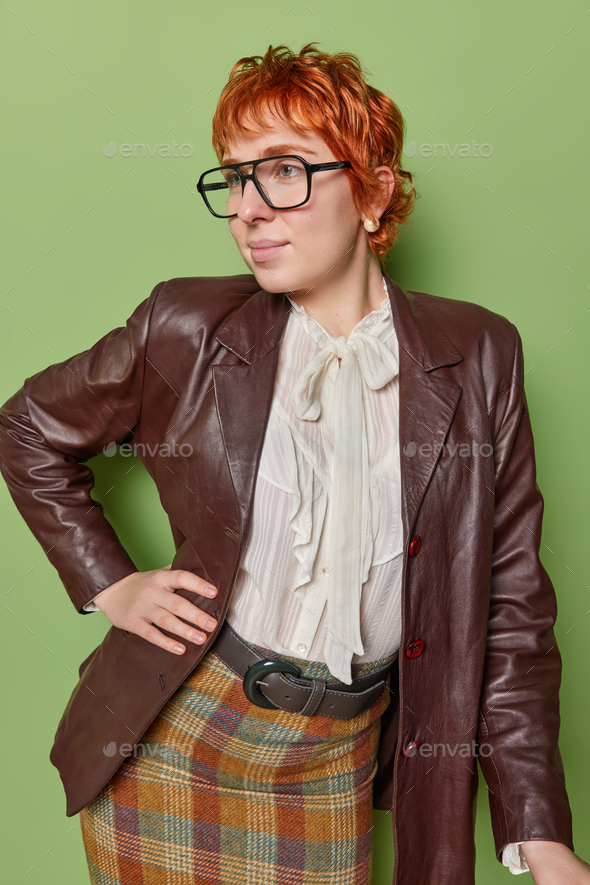 Indoor shot of thoughtful redhead lady dressed in elegant clothes keeps