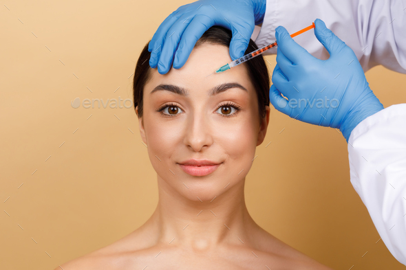 Injection Cosmetology. Beautician Doctor Making Botox Shot To Young Indian Woman Forehead
