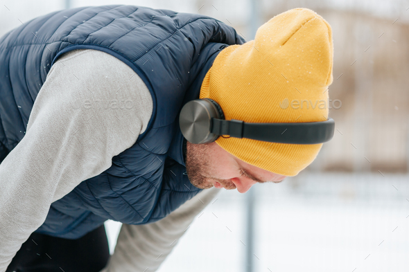 A male with headphones he looks tired, he leans down athlete braves the winter weather