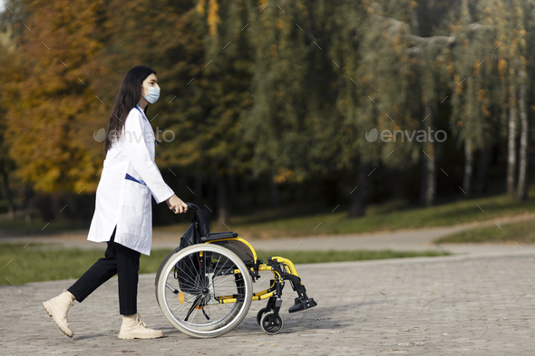 Caring young doctor in a protective mask carries a wheelchair. A young nurse is carrying a cart