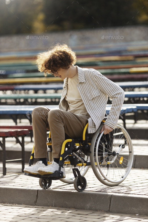 Concentrated, young man in a wheelchair is trying to go down the stairs