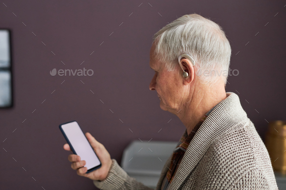 Elderly man with hearing aid listening audio on smartphone