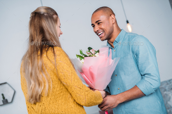 smiling african american boyfriend presenting bouquet to girlfriend