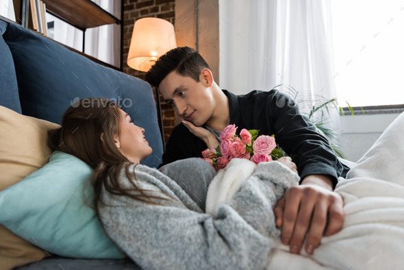 boyfriend presenting bouquet of roses to girlfriend in bed on international womens day
