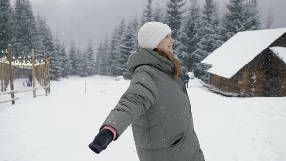 Happy Woman Enjoying the Snowfall Whirling in a Winter Forest in the Mountains alt