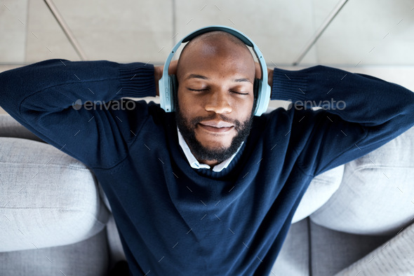 Top view, music headphones and black man on sofa in home living room streaming audio. Meditation, r