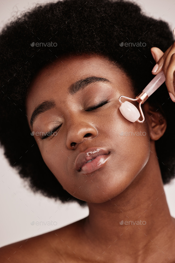 Black woman, skin care and facial roller for face massage in studio with dermatology and cosmetic t