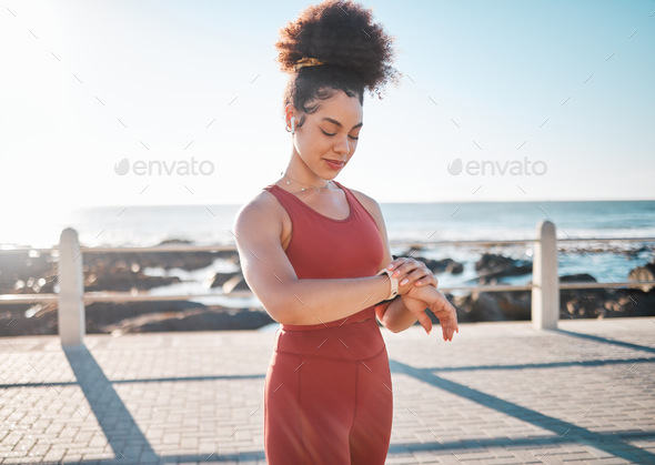 Fitness, black woman and watch checking by beach for time, performance or tracking exercise in the