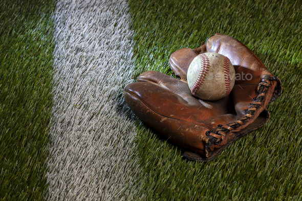 Old baseball in brown leather mitt on a grass field with a white stripe