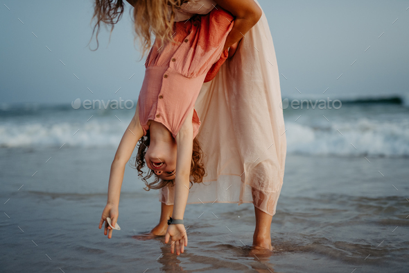 Mother holding her daughter upside down, enjoying summer vacation, having fun.
