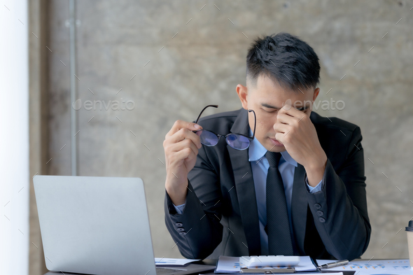 Asian businessman is stressed and eye strain and tired due to long working day on laptop computer