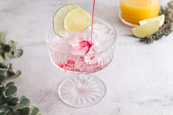 Faceted cocktail glass with crushed ice and lime into which grenadine syrup is poured close up