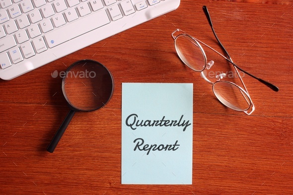 Magnifying glass, glasses, keyboard and blue paper with text QUARTERLY REPORT.