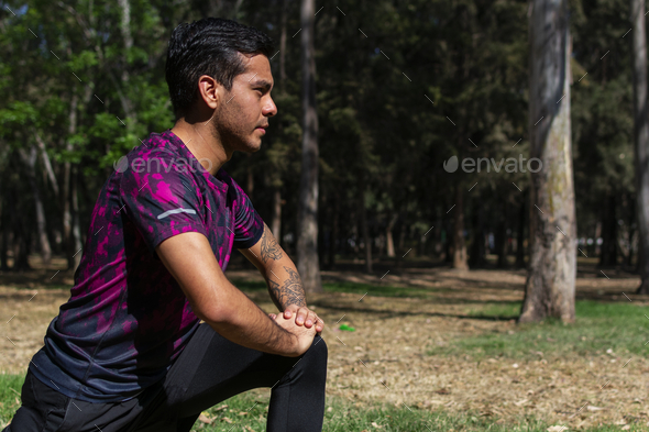 Hispanic man with a tattoo sleeve wearing a sportswear and stretching at the park