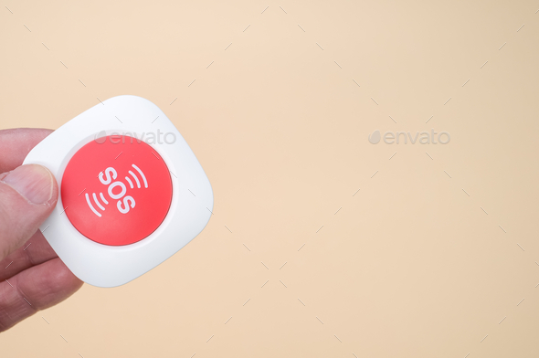 Elderly hand holding a wireless SOS emergency alarm button isolated on light brown background