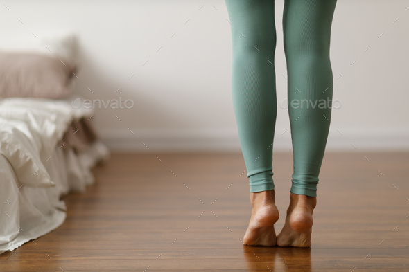 Young woman in sports leggings walks barefoot on the warm floor in the  bedroom. Stock Photo by atercorv