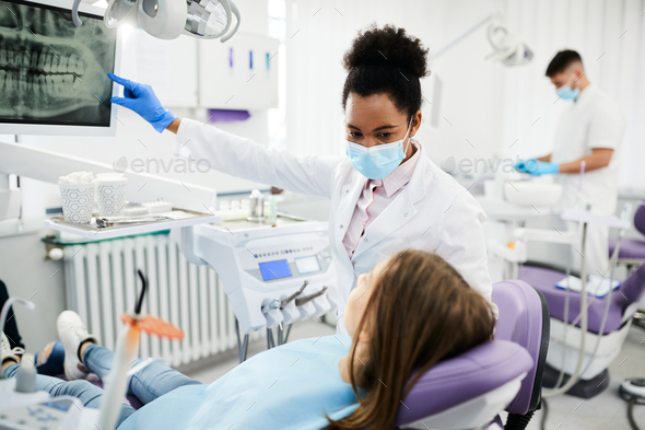 Black female dentist explaining dental X-ray to teenage patient at dental  clinic. Stock Photo by drazenphoto