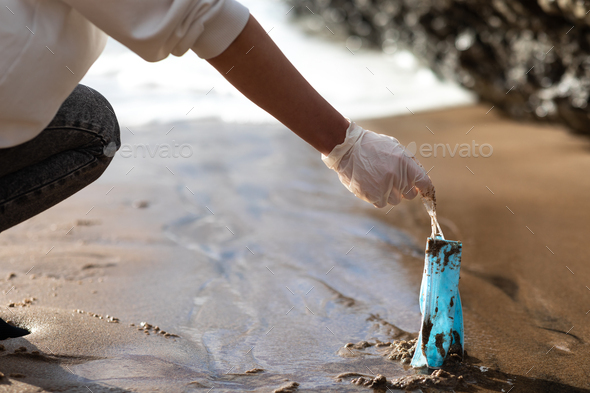 Female volunteer picking up used disposable medical face masks on the beach, cleaning coastal zone