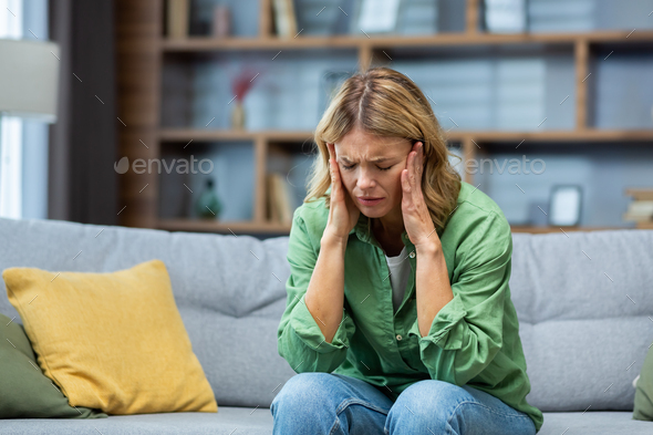 Mature woman alone at home with boss and depressed, housewife sitting upset on sofa holding head