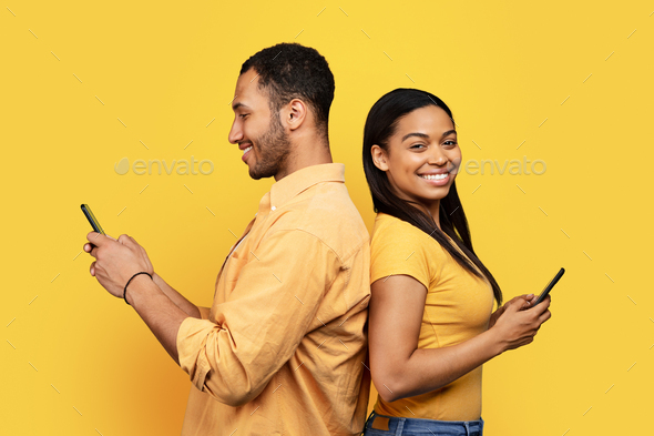 Smiling young african american family back to back, chatting on smartphones