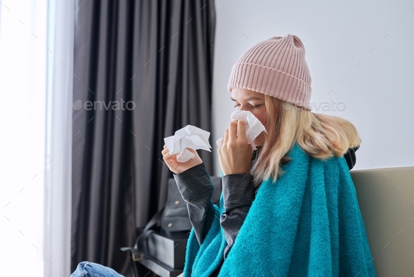 Teenager girl sneezing in handkerchief, female with symptoms of illness sitting at home