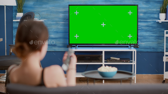 Static tripod shot of young woman switching channels while looking at green screen on tv