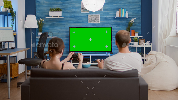 Static tripod shot of young woman and boyfriend gaming online having fun on green screen