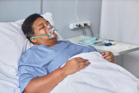 Black senior woman laying on bed in hospital room with oxygen support
