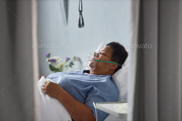 African American woman laying on bed in hospital room with oxygen support mask