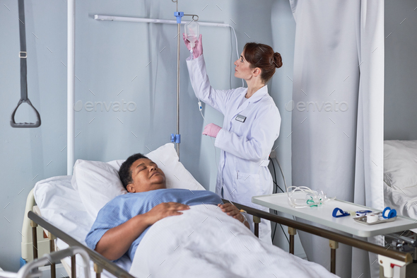 young nurse setting up IV therapy for senior woman in hospital bed