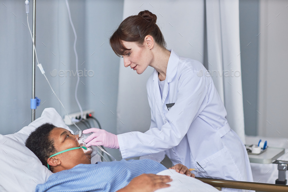 Caring nurse placing oxygen support mask on senior patient in hospital room