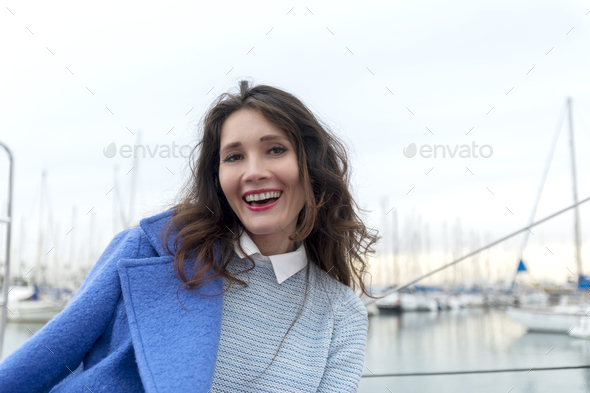 Beautiful woman in pink dress and blue jacket posing on a sailboat in a city harbor on a cloudy day. - Stock Photo - Images