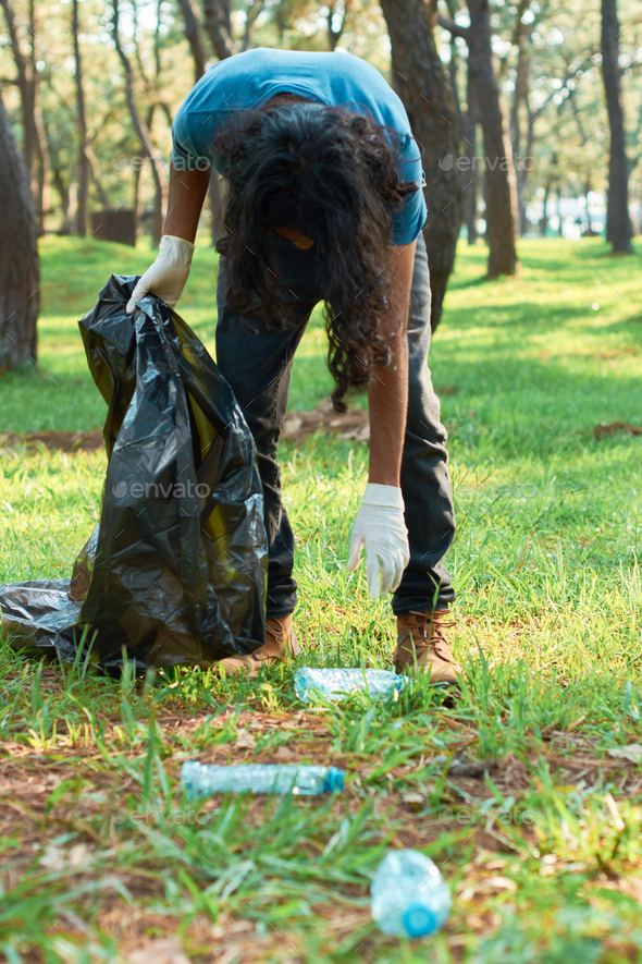 Latino teenage male volunteer picks up trash from the forest for plastic recycling.