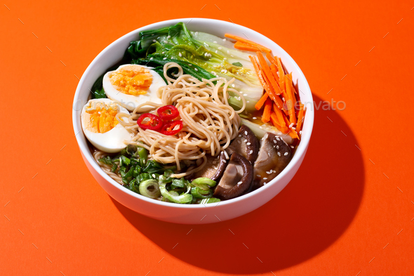 Ramen noodle soup with eggs, mushrooms, pak choi in hard light on orange