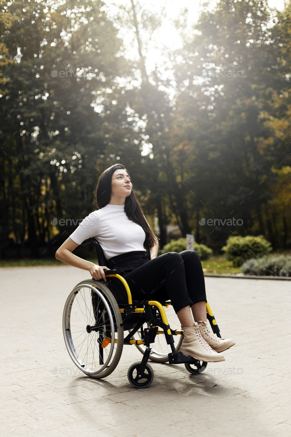 Charming disabled woman sits in a wheelchair. Attractive girl raised her head, looking up