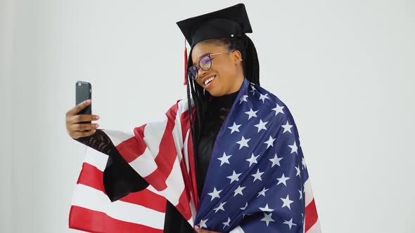 Happy Stylish Afro American Female Student in Graduate Uniform Taking Selfie Holding USA Flag on alt