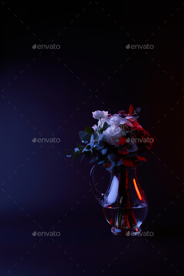 bouquet of different flowers in glass carafe with water on dark