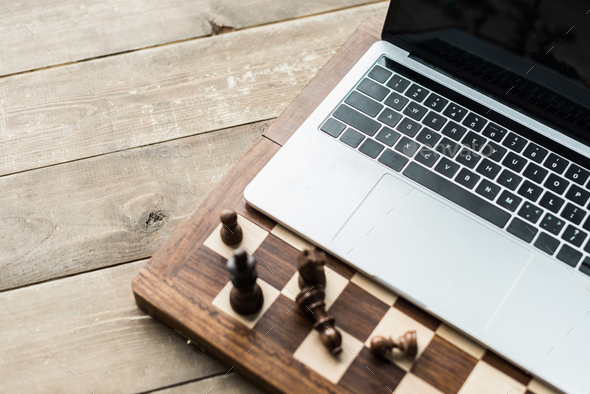 Chess board with chess pieces and laptop on rustic wooden surface