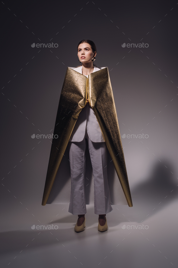 stylish woman in white suit covered in golden wrapping paper posing on dark background