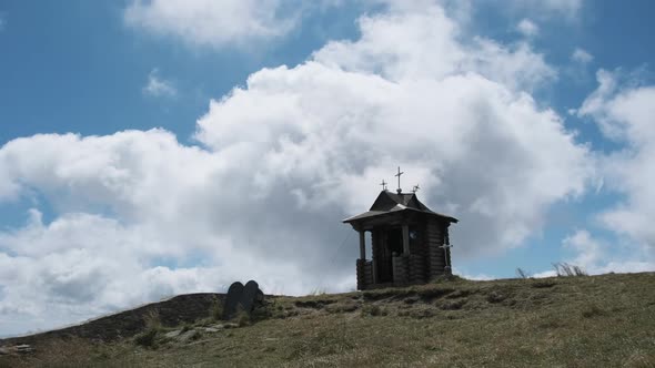 Small Old Wooden Chapel on Top of Mountain on Background Moving Clouds in Sky. alt